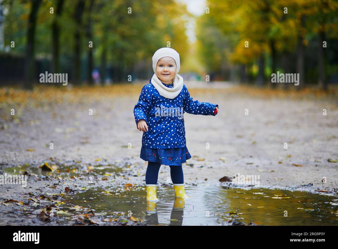 Child wearing yellow rain boots and jumping in puddle on a fall day ...
