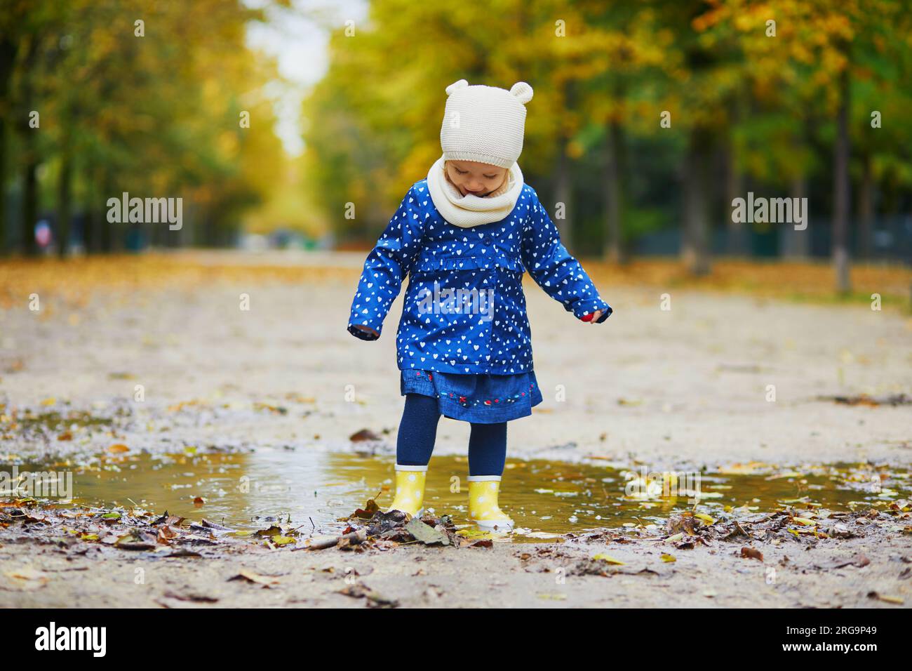 Child wearing yellow rain boots and jumping in puddle on a fall day ...