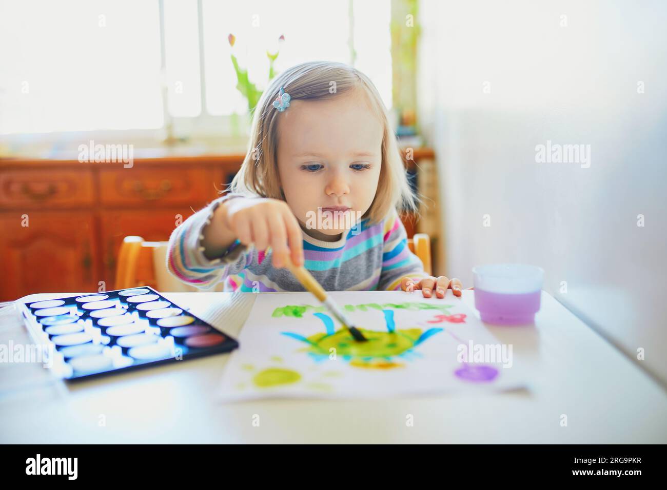 Adorable little girl painting with aquarelle at home, in kindergaten or preschool. Creative games for kids staying at home Stock Photo
