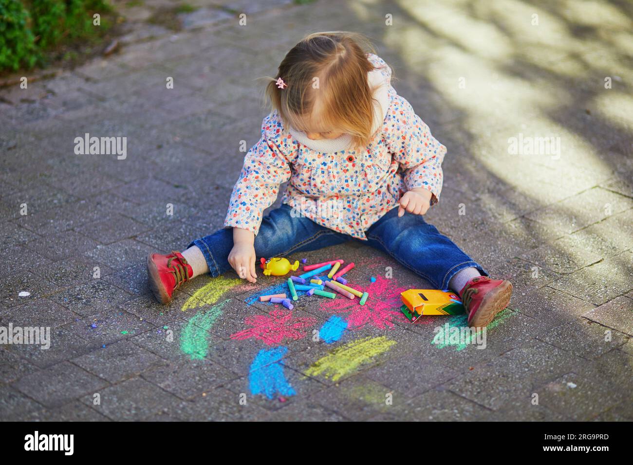 Adorable toddler girl drawing with colorful chalks on asphalt. Outdoor ...