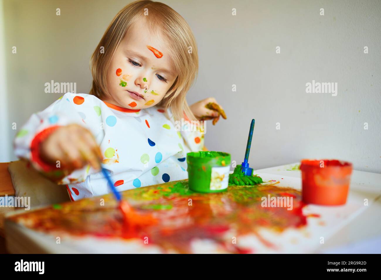 Adorable little girl with paint on her face painting with brushes and