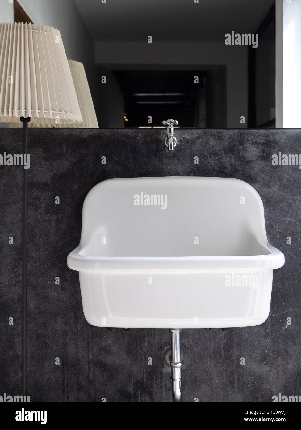 Empty big white vintage medical wall mount bathroom sink on black concrete wall decoration near big mirror and standing light lamp in the bathroom, ve Stock Photo