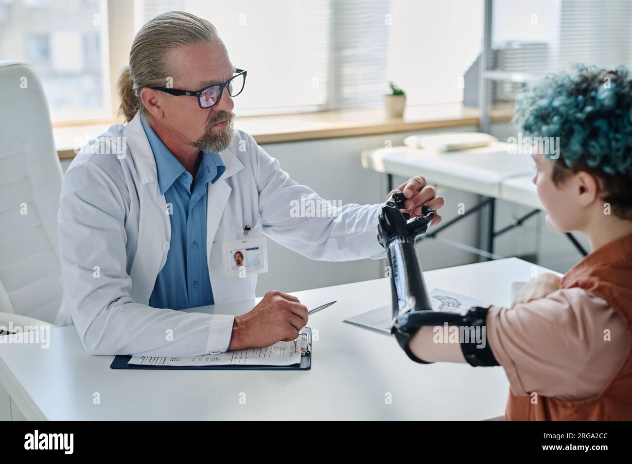 Portrait of senior prosthetist consulting young woman with artificial arm in orthology clinic Stock Photo