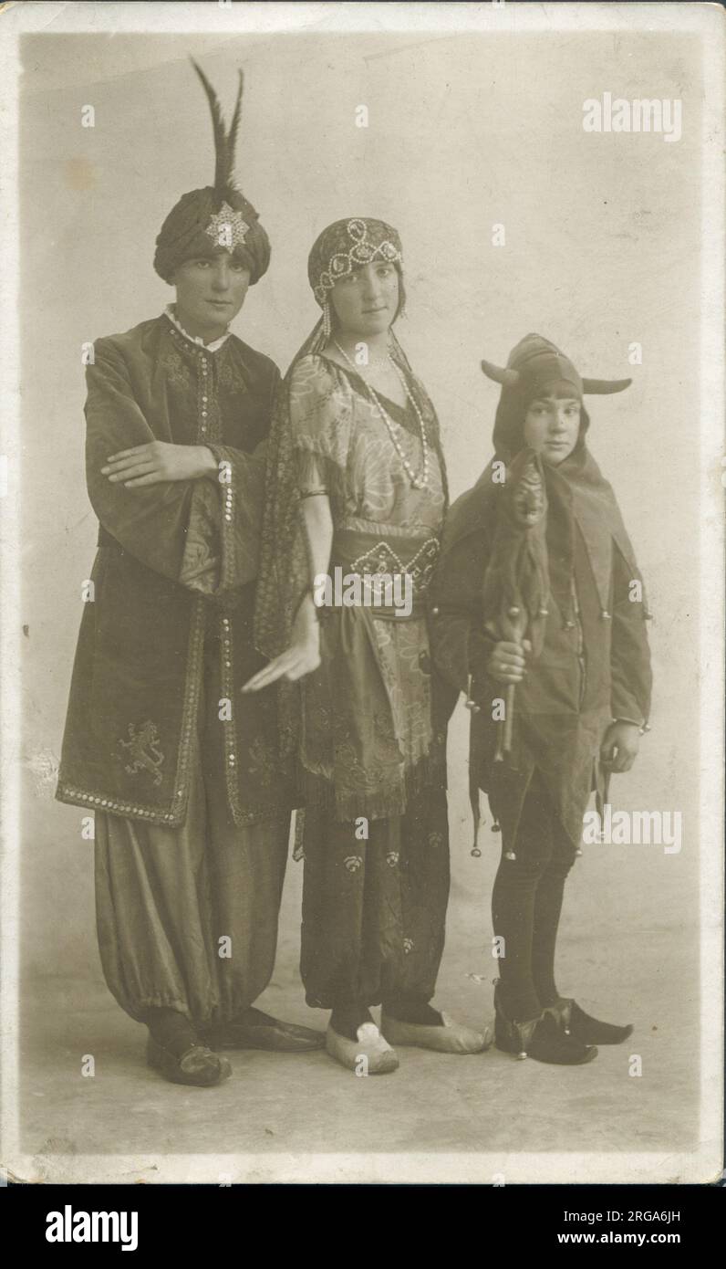 Three people in fancy dress; two adults in exotic 'Arabian Nights' style outfits, while a little boy (or girl?) appears to be dressed as a medieval jester or similar. Stock Photo