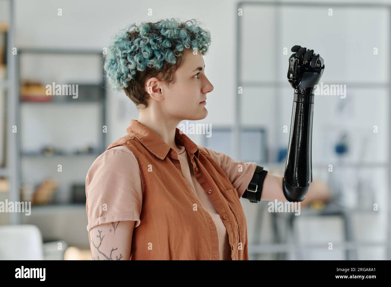 Side view portrait of young woman looking at cyber prosthetic arm and smiling Stock Photo