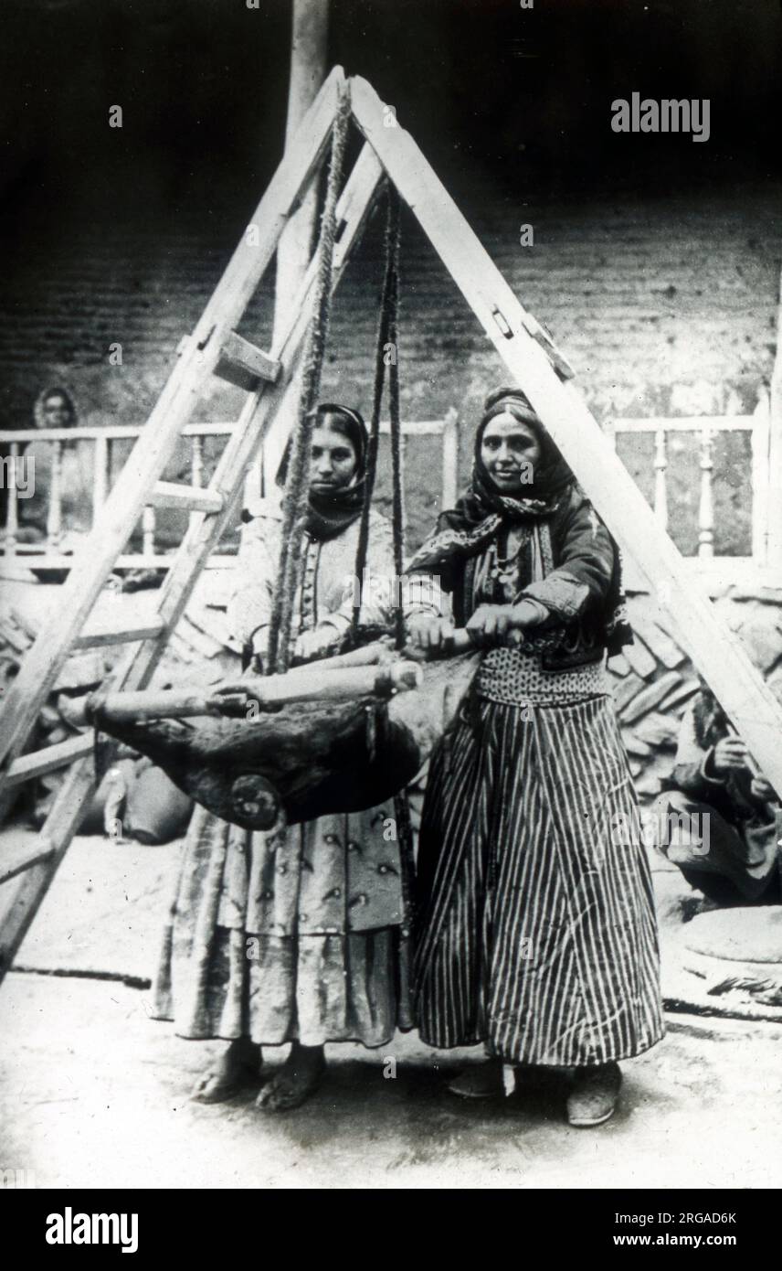 Two Persian women rocking a goatskin to churn milk. Stock Photo