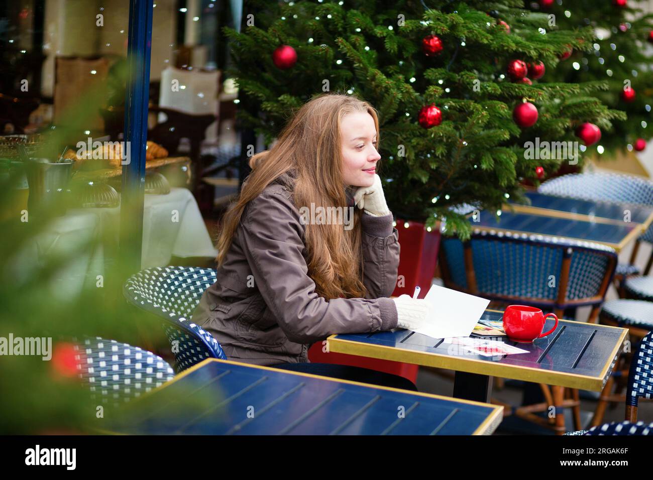 Girl writing Christmas postcards in an outdoor Parisian cafe Stock Photo