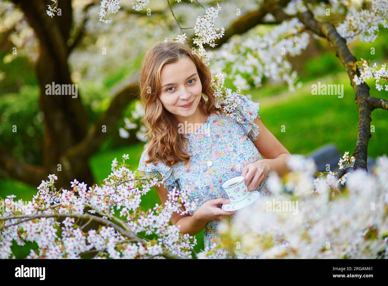 Beautiful young girl drinking tea in cherry garden on a spring day ...