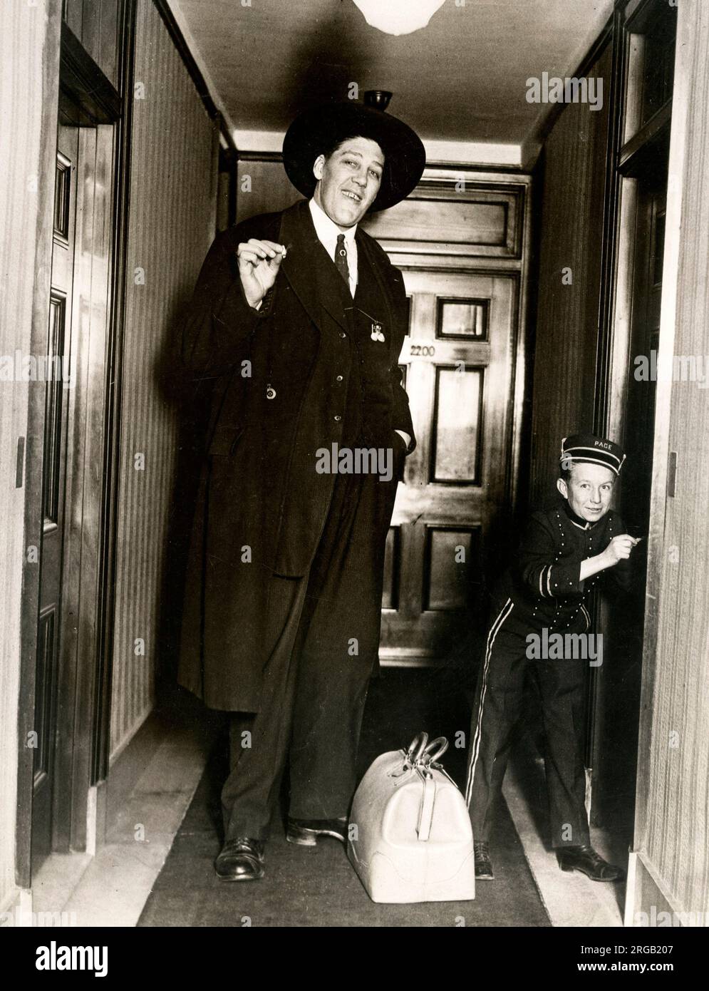 Early 20th century vintage press photograph - tall actor John Aasen and dwarf bellhop in New York, 1924. John Aasen (March 5, 1890 - August 1, 1938) was an American silent film actor and sideshow performer who was one of the tallest actors in history. Stock Photo
