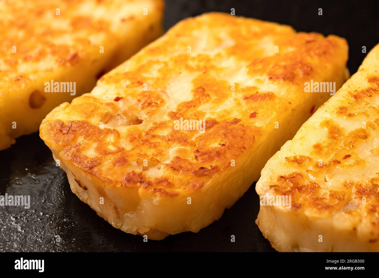 Detail of fried slices of halloumi cheese with red chilli on black frying pan. Stock Photo