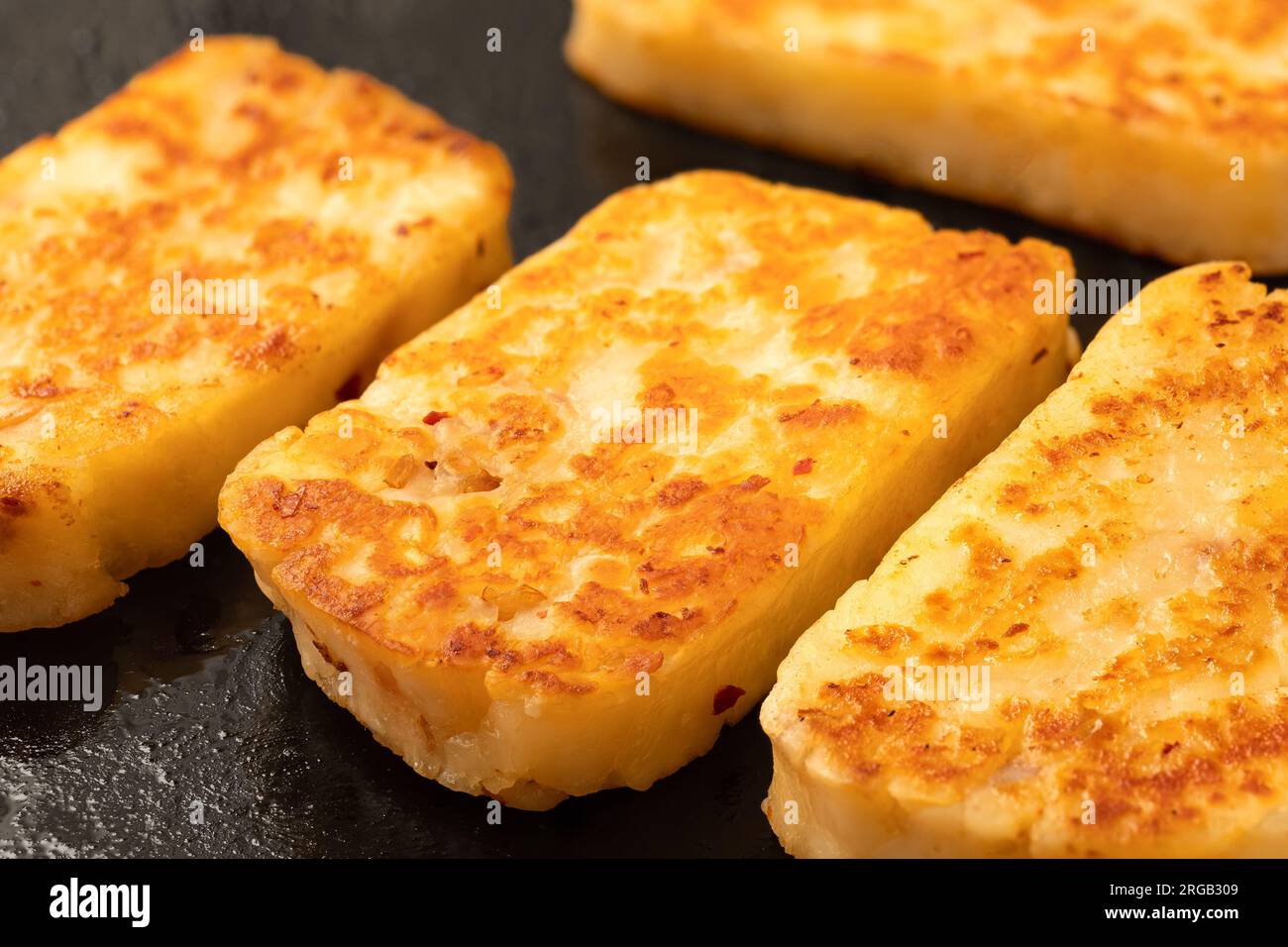 Detail of fried slices of halloumi cheese with red chilli on black frying pan. Stock Photo