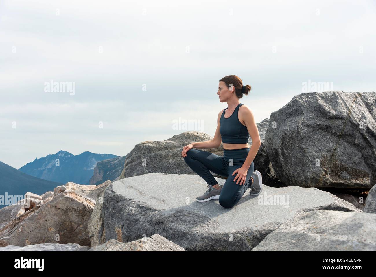 Fit woman runner, kneeling on rocks, running up a mountain Stock Photo