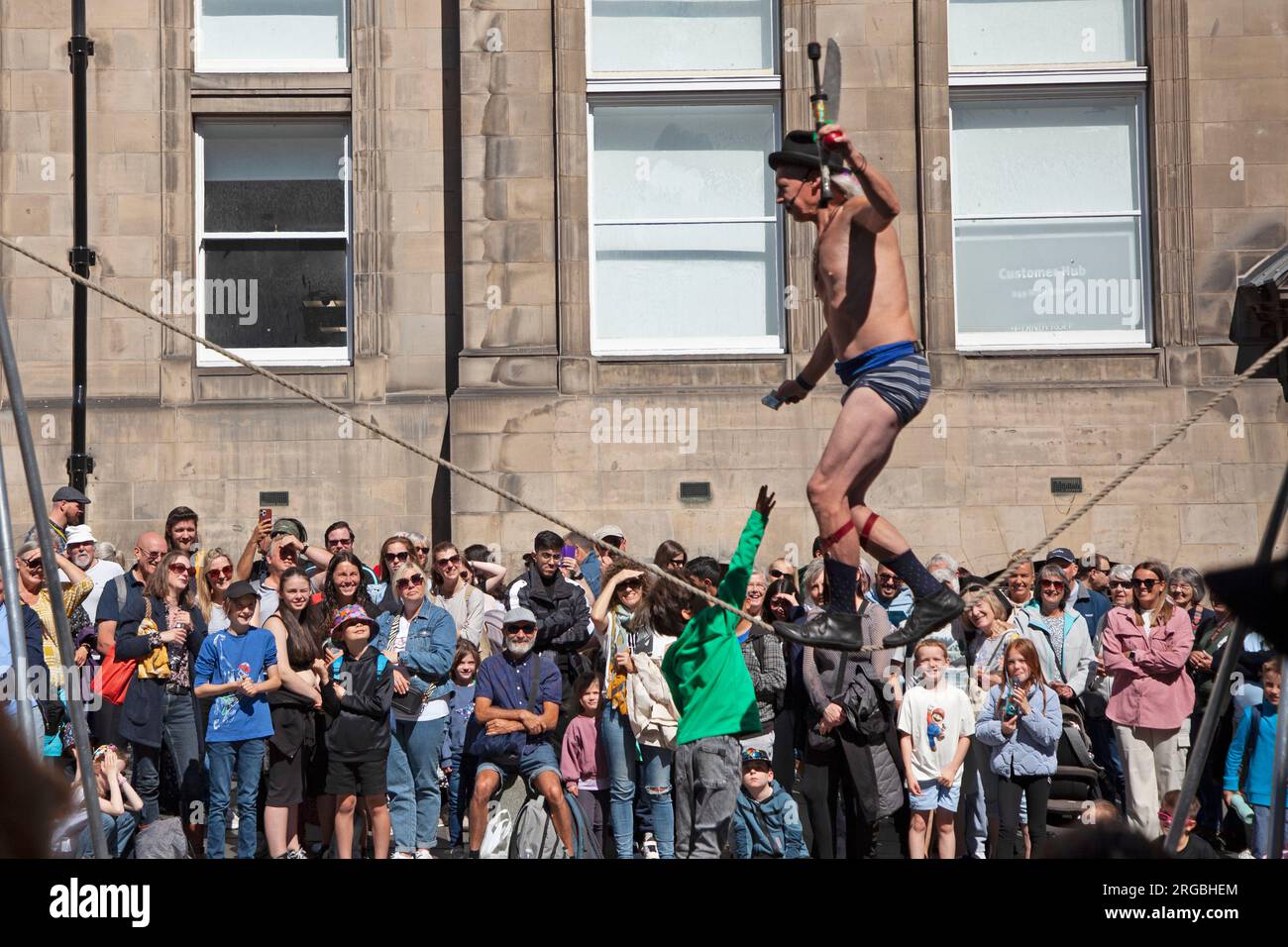 Royal Mile, Edinburgh, Scotland, UK. Busy day at Edinburgh Fringe Festival, large audiences stopping to watch and be entertained by Street Performers on the High Street, helped by the sunshine and warmer weather. Pictured: Kwabana Lindsay Street Performer tease a youn boy with a fiver for assisting him. Credit: Archwhite/alamy live news. Stock Photo
