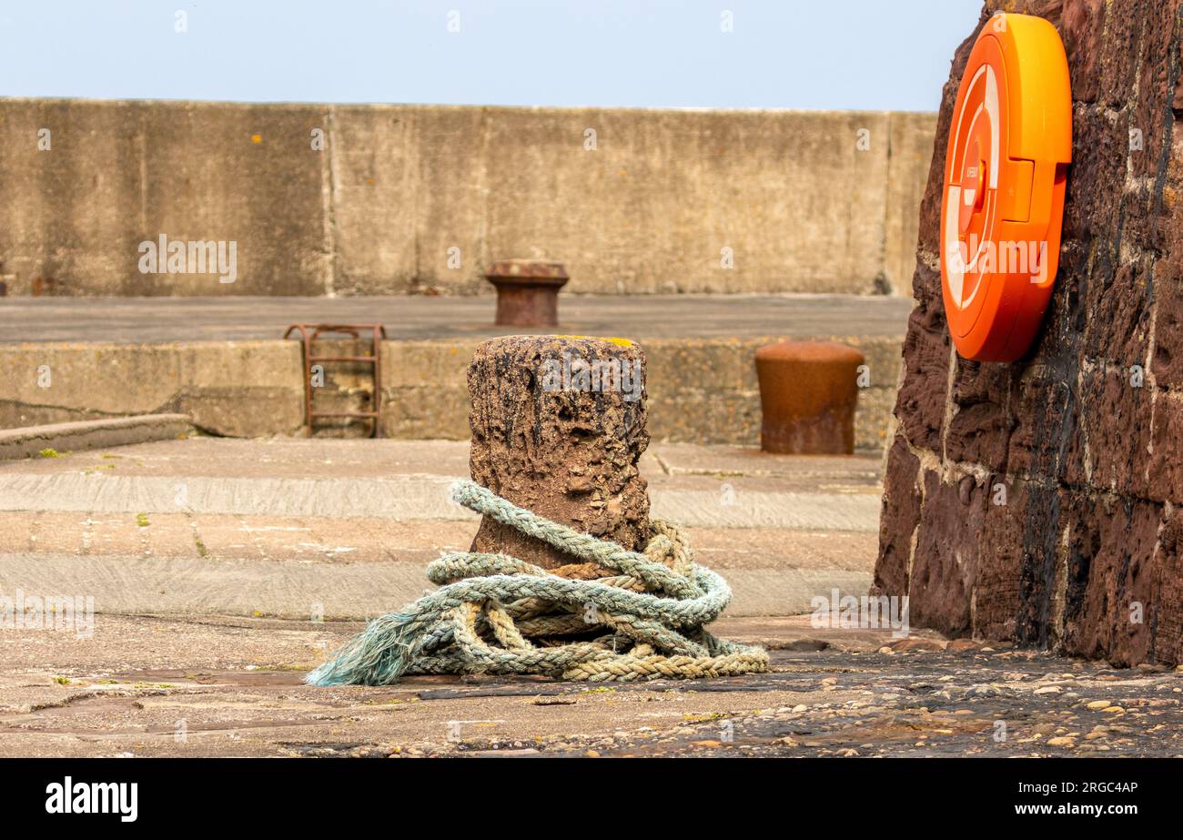 Harbour side with rope around old concrete support and life safety ring Stock Photo