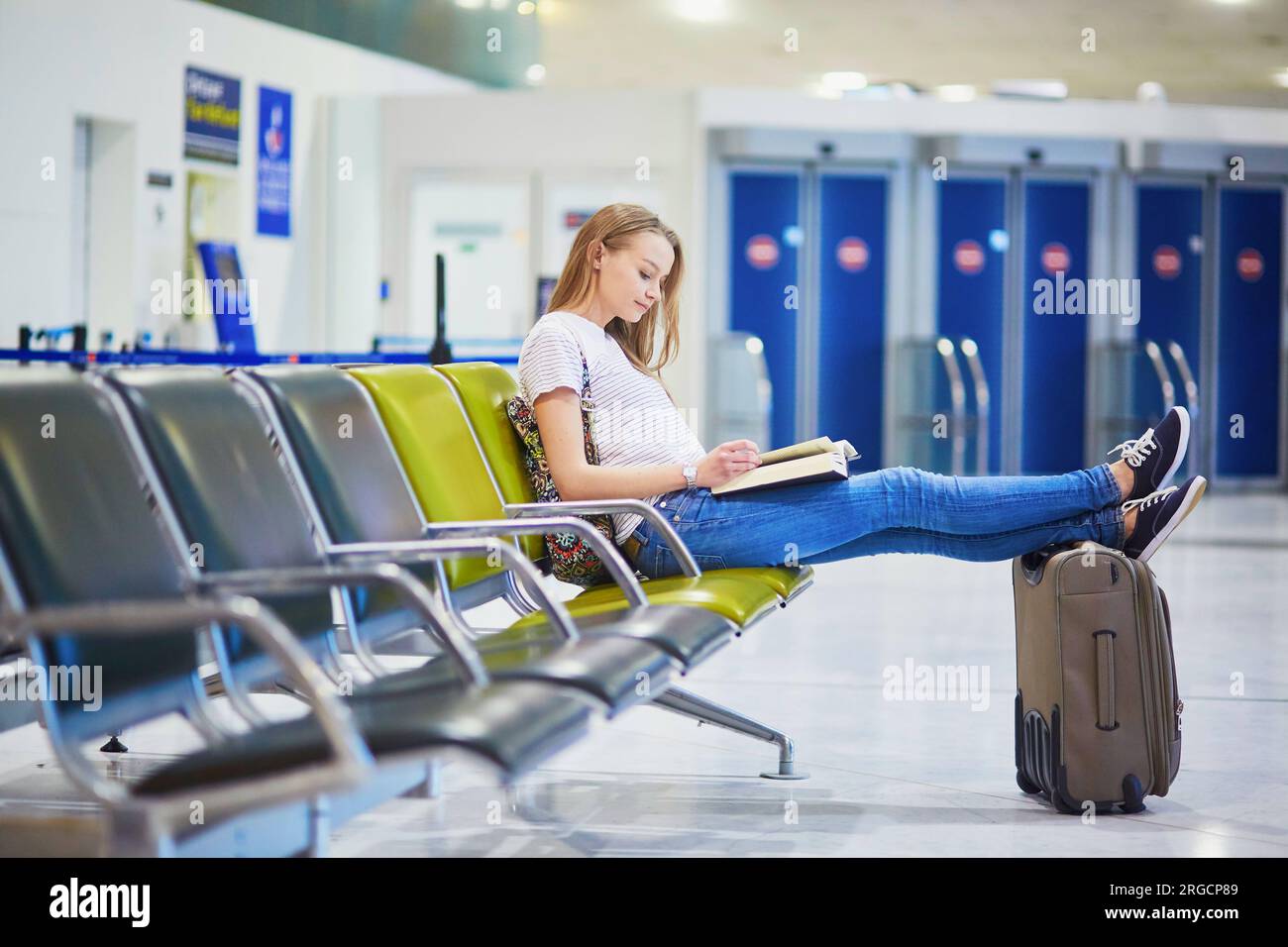Young traveler with carry on luggage in international airport reading a