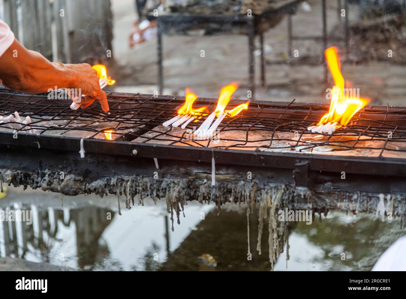 Large bright flames from burning candles,molten candle wax dripping from metal tray as people place and position them carefully as they pray to Jesus Stock Photo