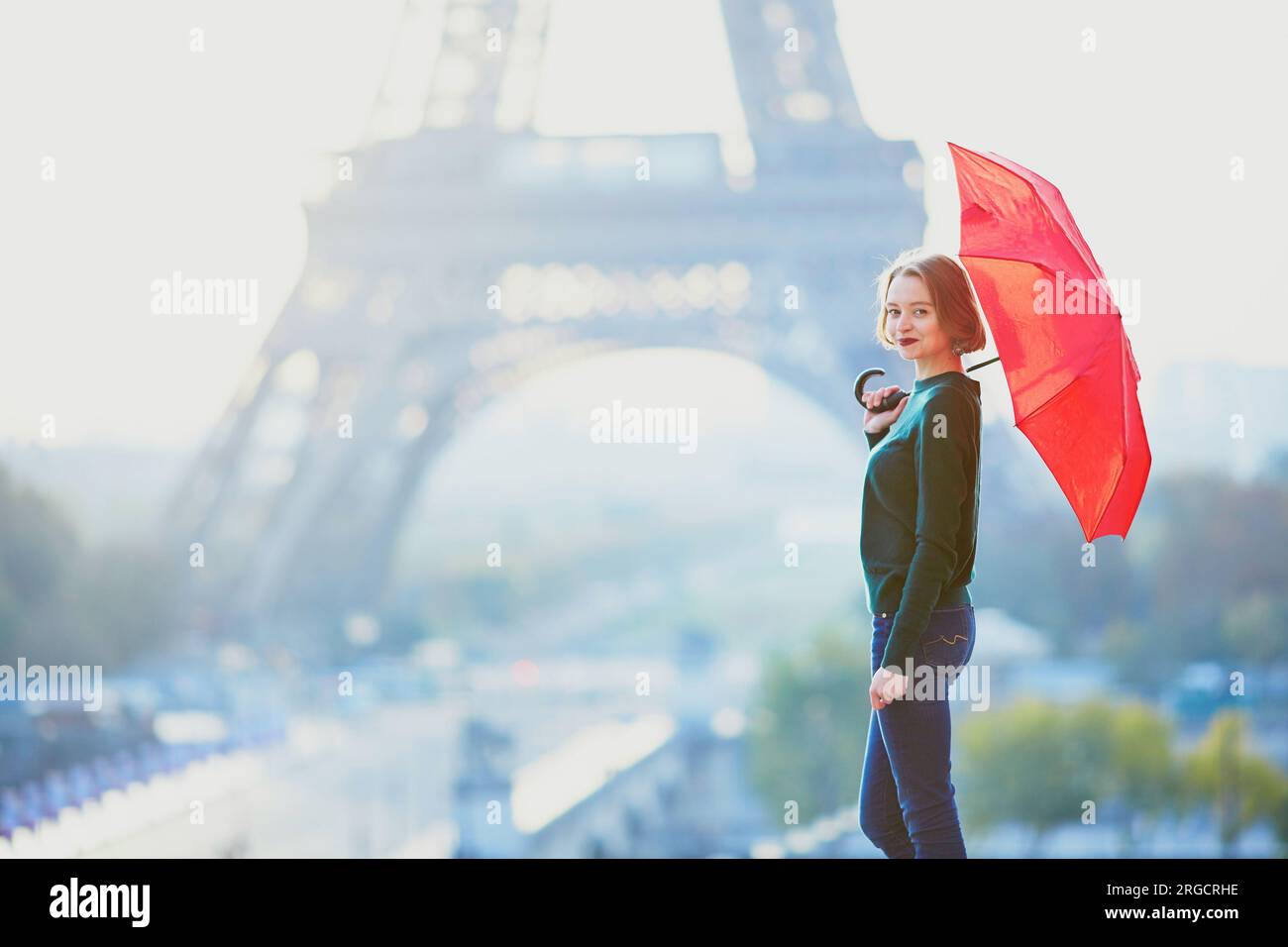 Beautiful young girl with red umbrella in Paris near the Eiffel tower