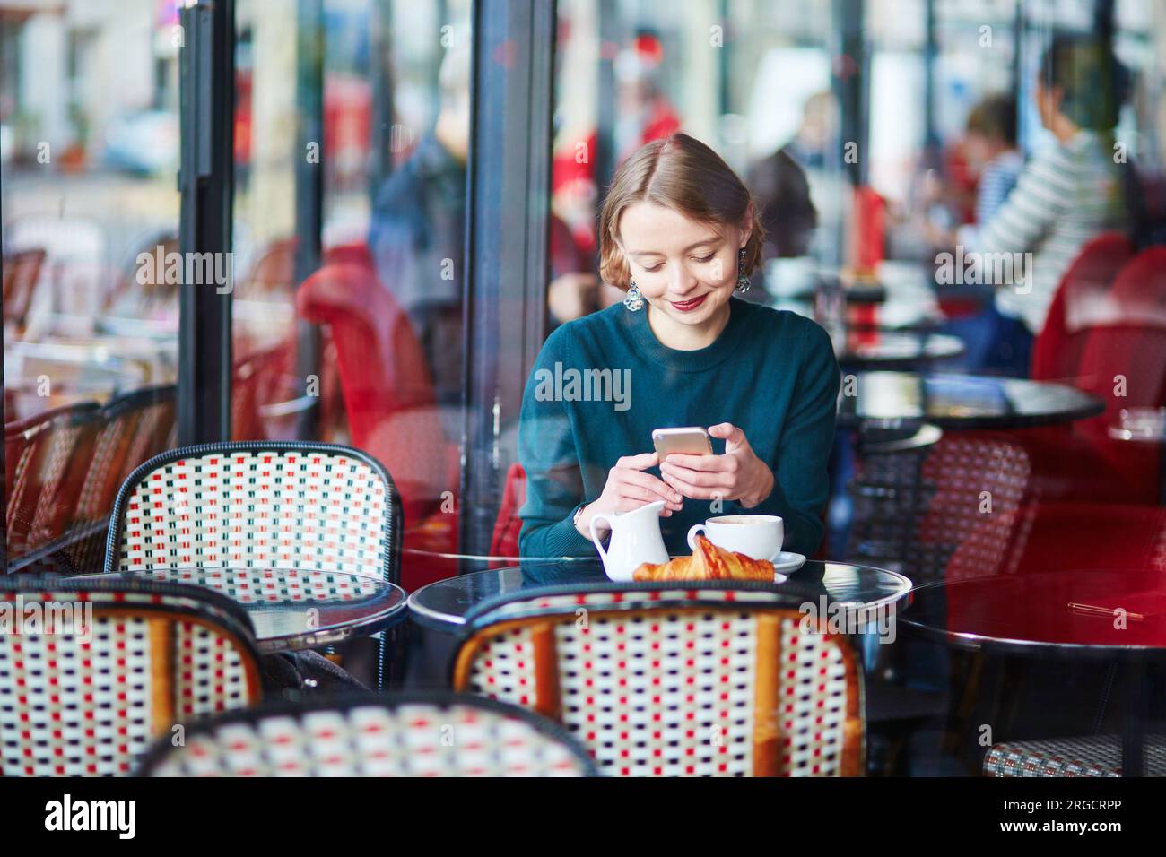 Young elegant woman drinking coffee and using her mobile phone in traditional cafe in Paris, France Stock Photo