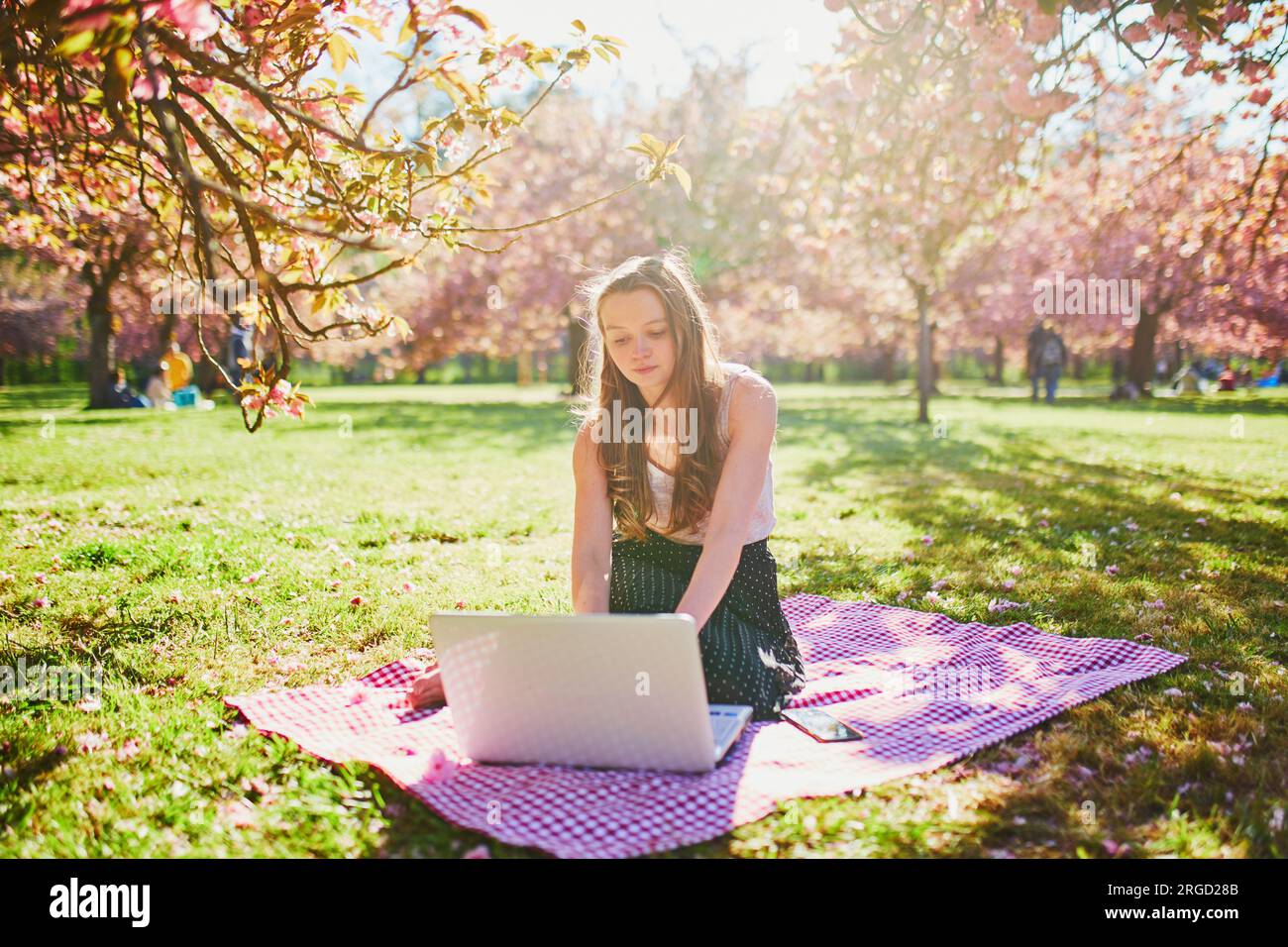 Beautiful young girl working on her laptop in park during cherry ...