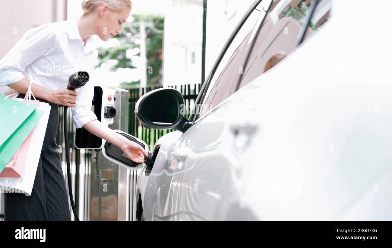 Progressive businesswoman unplug charger plug from charging station to his electric car before