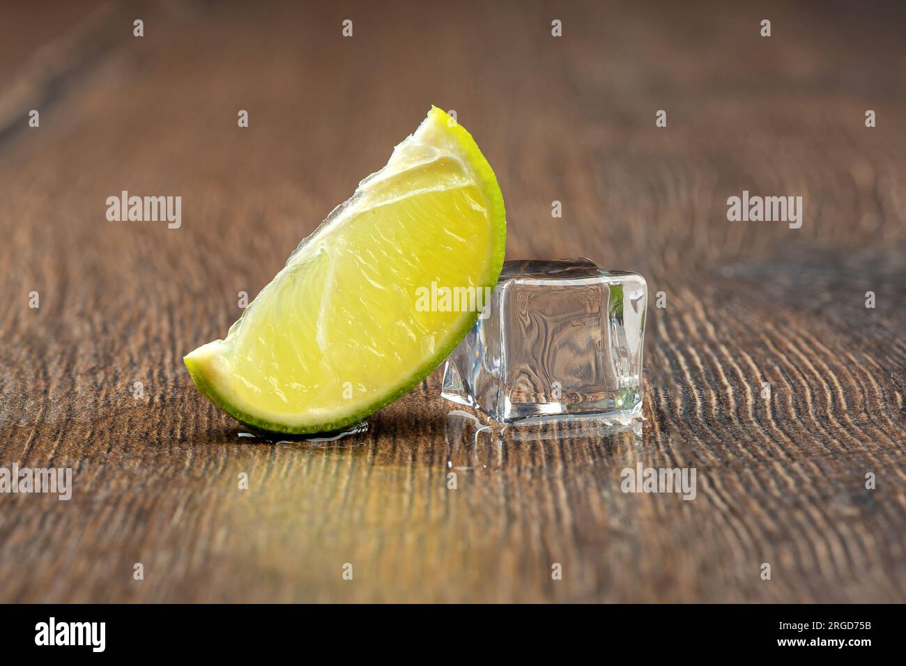 Slice of lime and a melting ice cube with drops of water on the table ...
