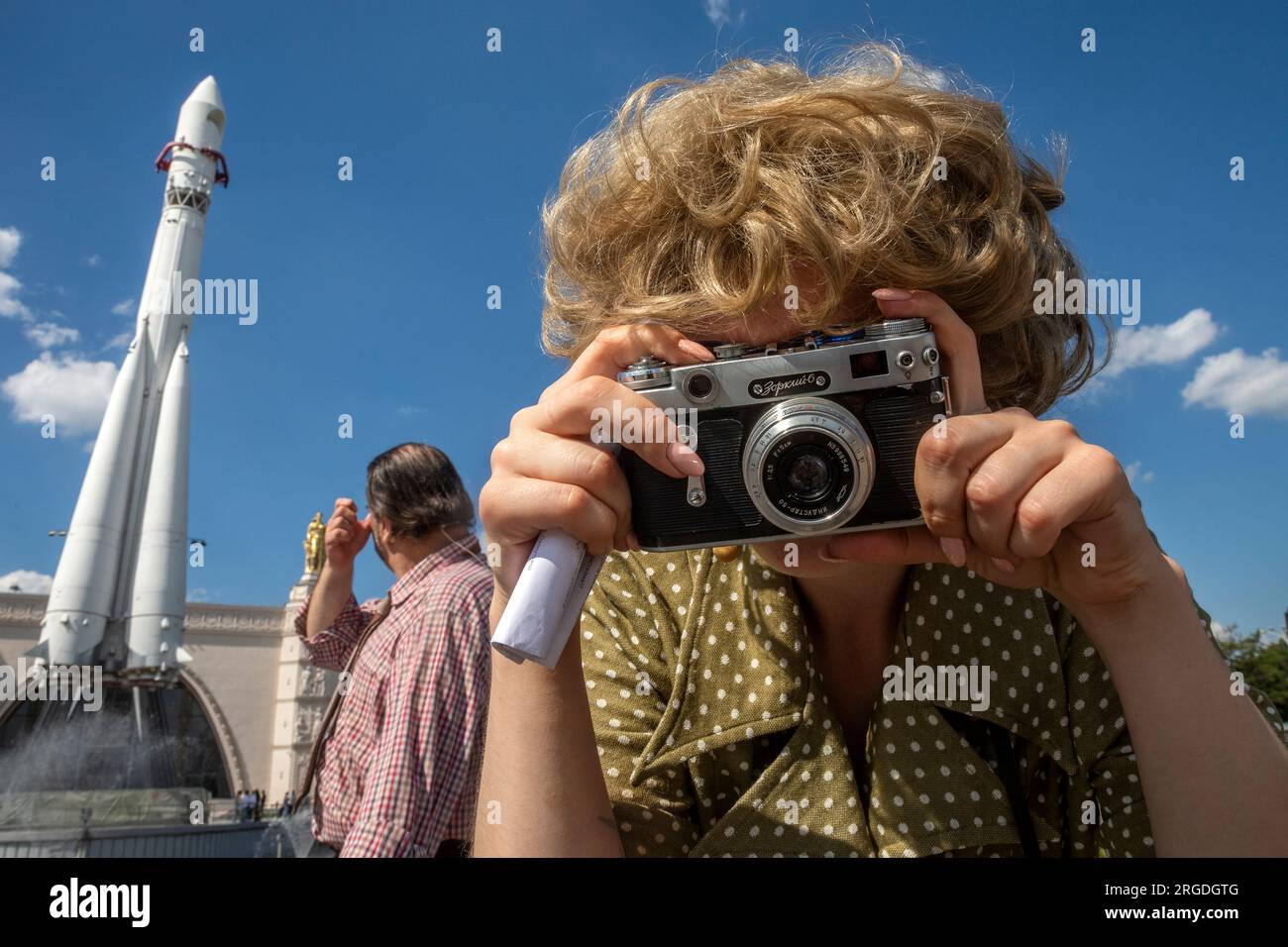 Moscow, Russia. 5th of August, 2023. A girl in clothes from the 1970s photographs with a Soviet camera Zorky-6 on the Industrial Square at the VDNH exhibition center in Moscow, Russia Stock Photo