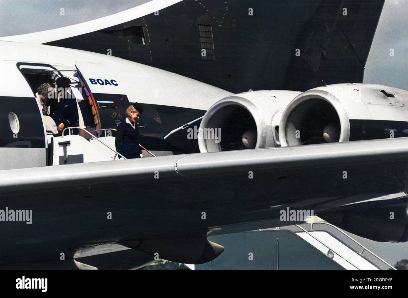 A happy, blonde air hostess leads the way for her passengers to leave an aeroplane at Manchester Airport, England. Stock Photo