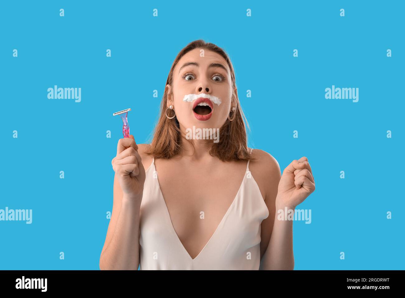 Shocked young woman with shaving foam and razor on blue background, closeup Stock Photo