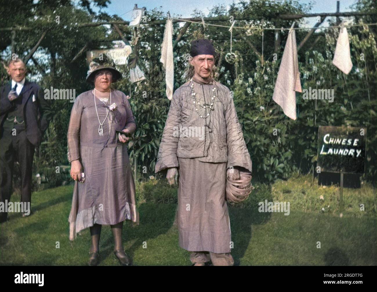 People in a garden, including a man in oriental costume and a Chinese Laundry sign on the right. Stock Photo