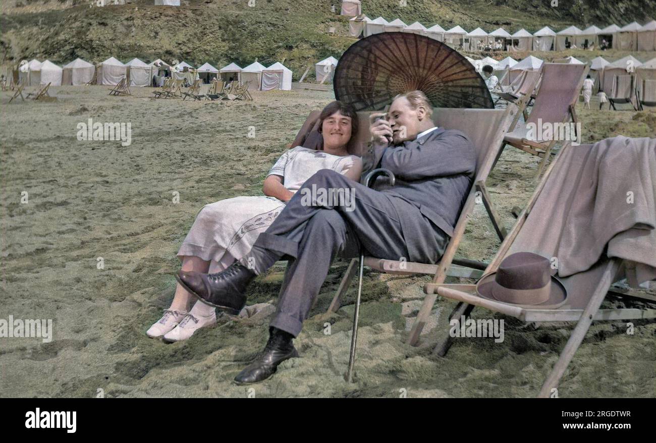 A man and a woman sitting in deckchairs on the beach at Newquay, Cornwall, with an oriental-style parasol to shade them from the sun. Stock Photo