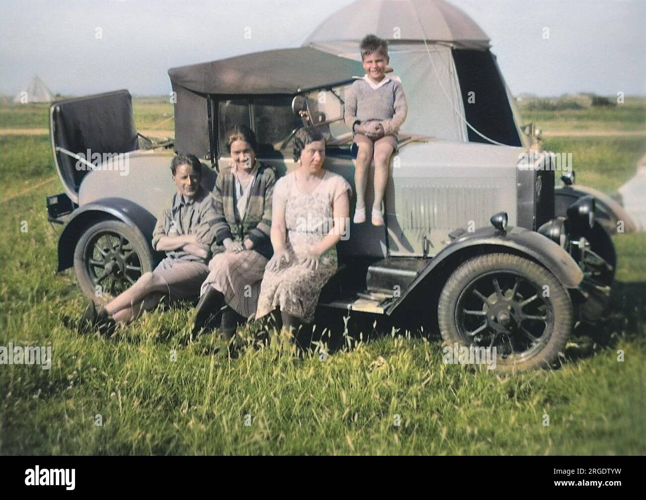 A family group of four, sitting on the running board of a car with a