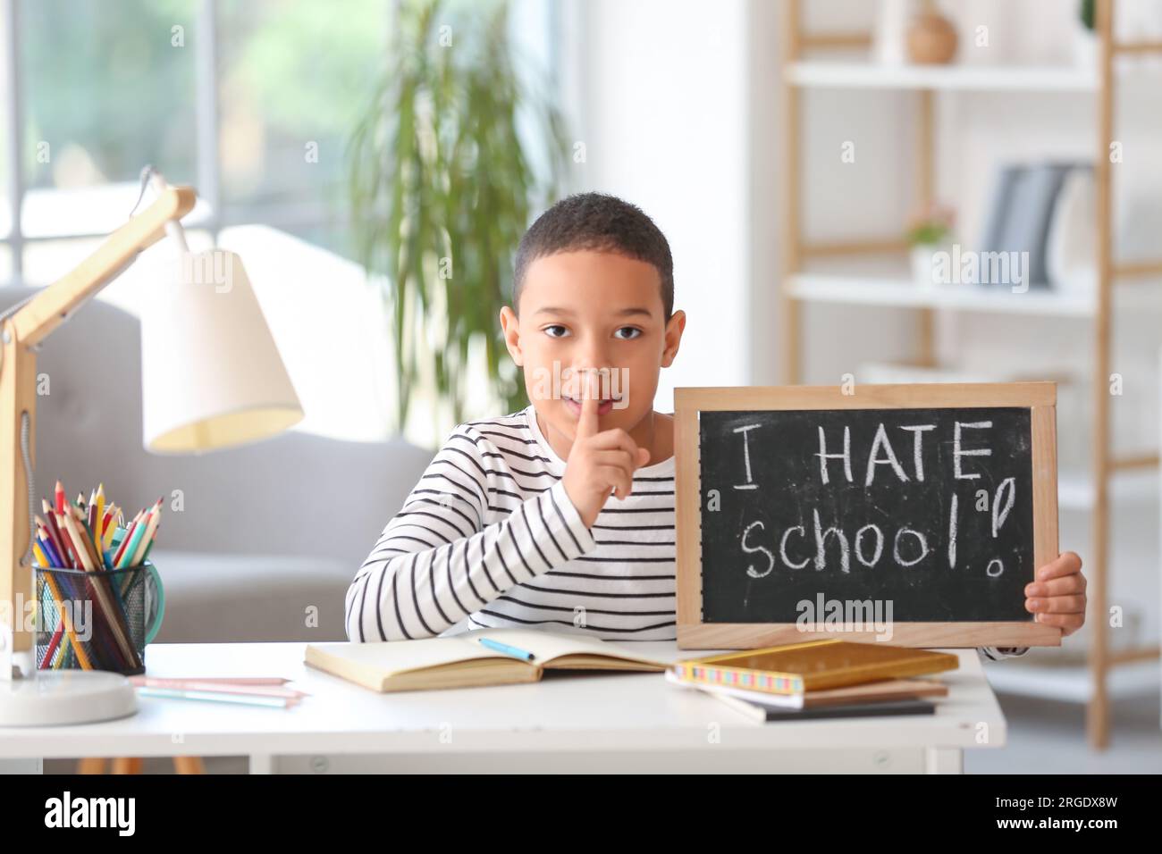 Little African-American boy holding chalkboard with text I HATE SCHOOL at home Stock Photo