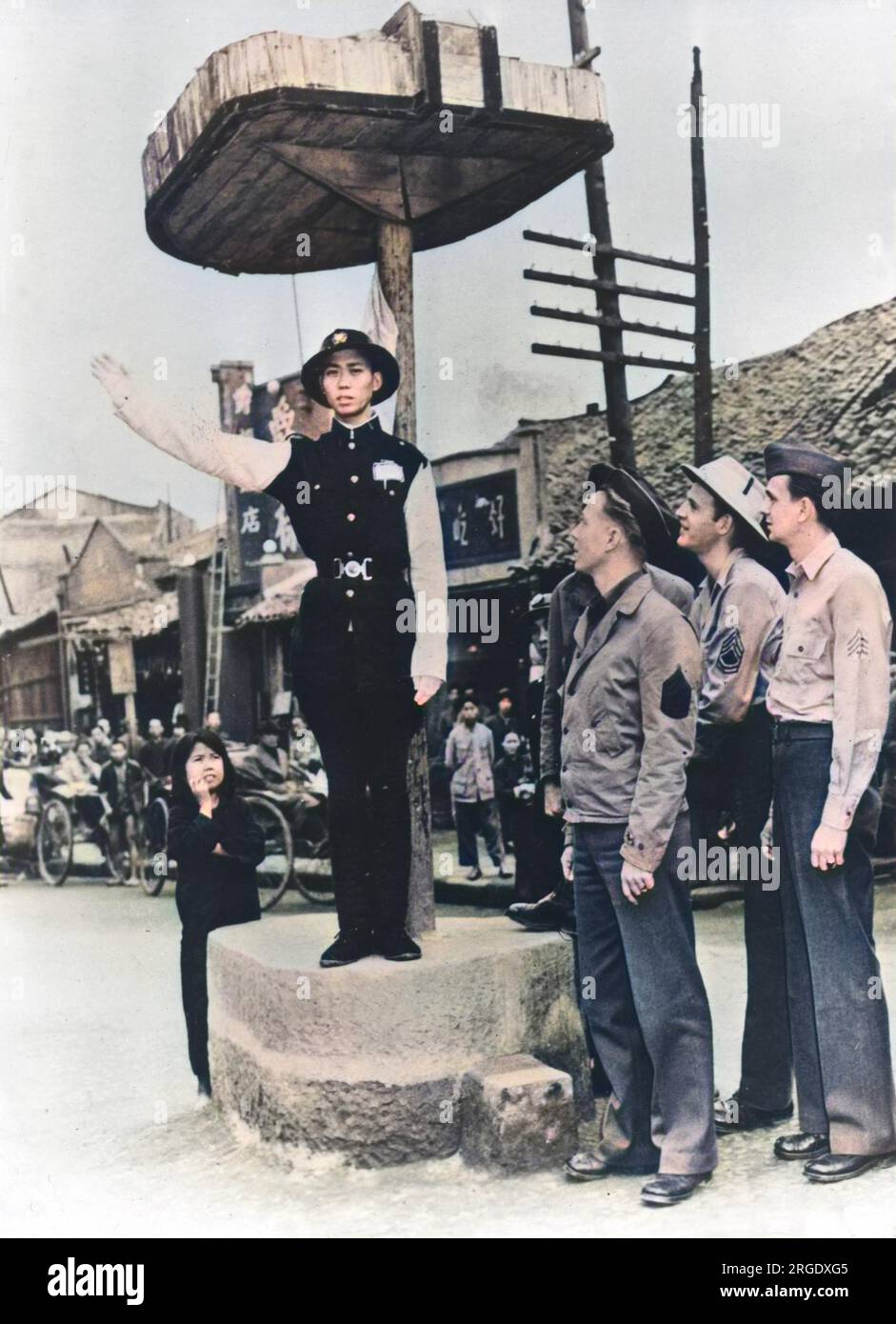American soldiers watch a Chinese policeman directing traffic somewhere in China in a town near a U.S. Army base Stock Photo