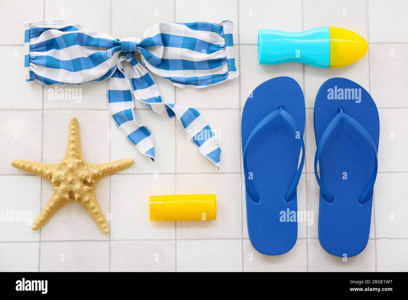 Pair of blue flip flops with swimsuit and sunscreen cream on white tile ...