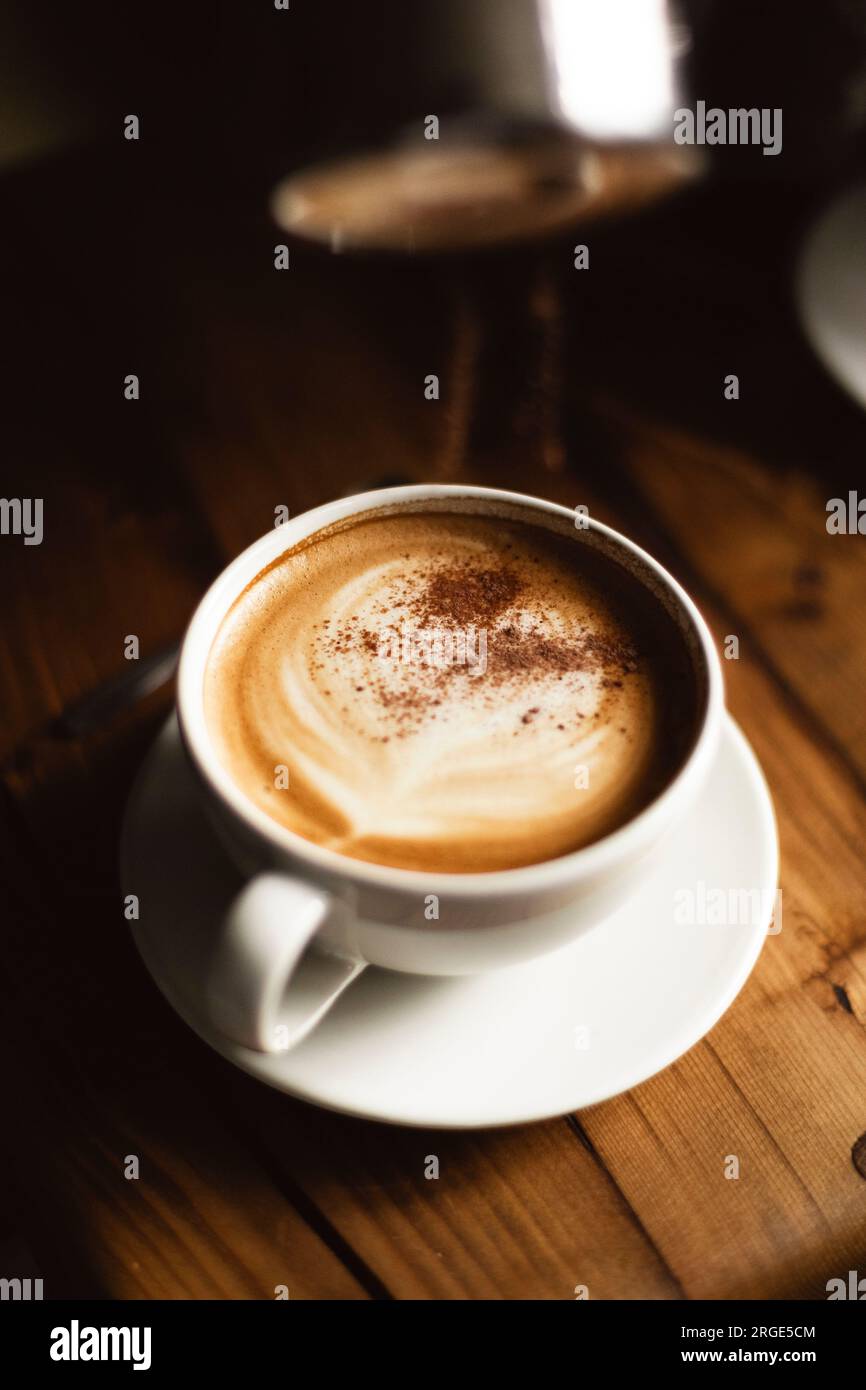 Cocoa powder sprinkled on coffee in white cup on wooden table Stock Photo