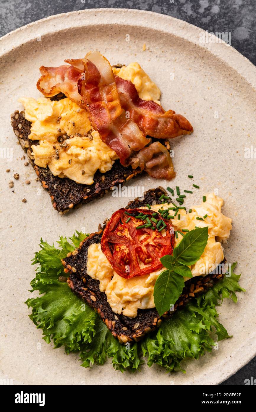 Scrambled eggs with bacon and tomato on toasted grain bread Stock Photo