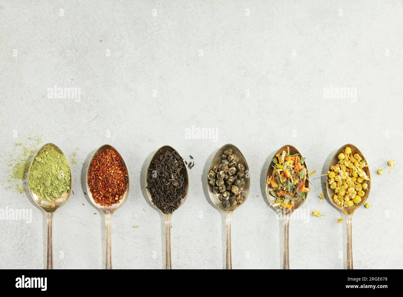 Different types of tea in vintage spoons. Flat lay, top view on concrete background. Matcha, rooibos, black, green, herbal mix and camomile tea. Copy Stock Photo