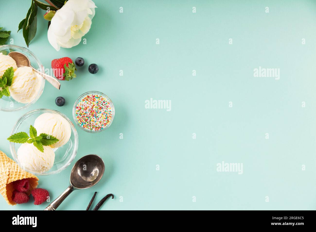 Scoops of Vanilla, mint leaves in glass bowl, sprinkles, berries and flowers over pastel light blue background, top view, banner, copy space. Summer m Stock Photo