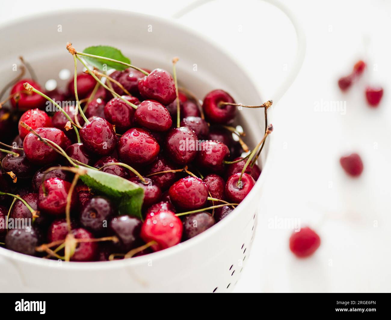 Fresh ripe cherries in white stainless steel colander. Close up view of wet red cherry over white woden background. Shallow DOF. Cherries aestetic. Co Stock Photo