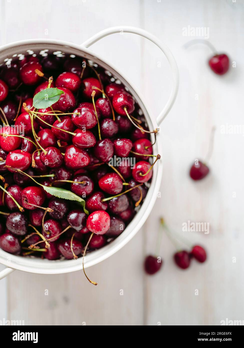 Fresh ripe cherries in white stainless steel colander. Top view of wet red cherry over white woden background. Shallow DOF. Cherries aestetic. Copy sp Stock Photo