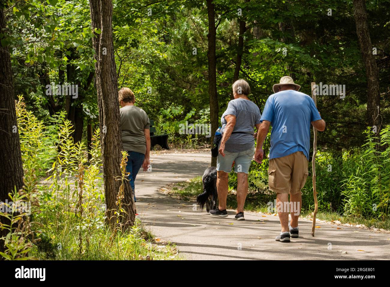 Two Caucasian women & a man walking with dog on a nature & exercise trail in Sedgwick County Park, Wichita, Kansas, USA. Stock Photo