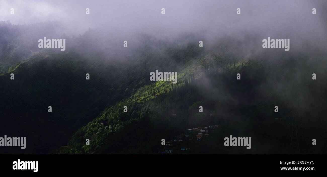 mist, monsoon clouds and darkness create dramatic landscape. beautiful mountain village on himalayan foothills near mirik in darjeeling, india Stock Photo