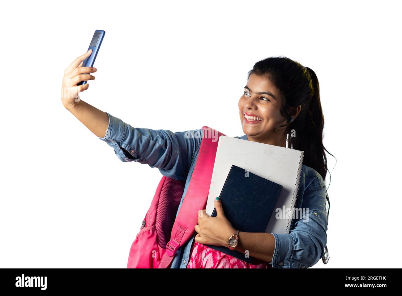 A pretty young Indian modern girl with books in hand taking selfie on white background Stock Photo