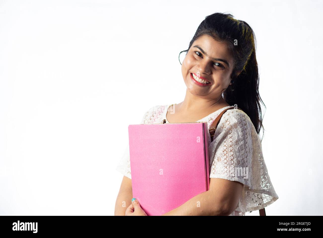 A pretty young Indian girl with books in hand standing with smiling ...