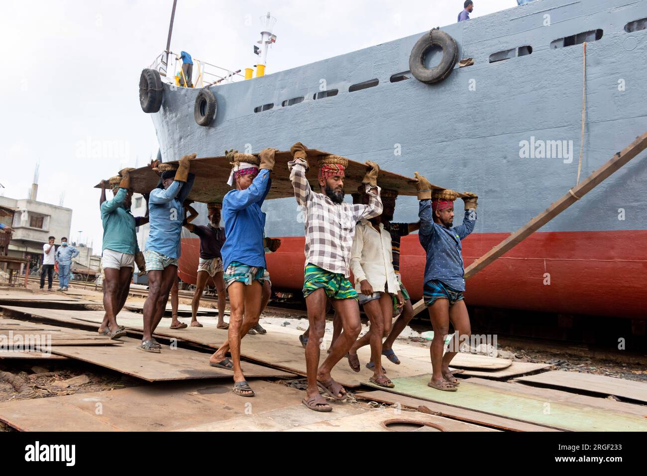 Dhaka, Dhaka, Bangladesh. 9th Aug, 2023. A group of porters carries a heavy steel plate of 250 kg at a dockyard on the bank of River Buriganga, in Keraniganj, near Dhaka, Bangladesh. Dozens of dockyards occupying 30.96 acres of the Buriganga foreshore have been in operation for the last 50 years. It is mostly utilized for fixing and repairing old ships, and build in new ships. Labors work in the dockyard without helmets, face masks, or safety shoes. They work hard all day long but are still paid minimum wages. With an increasing number of orders from both local and global buyers, the shipbuil Stock Photo