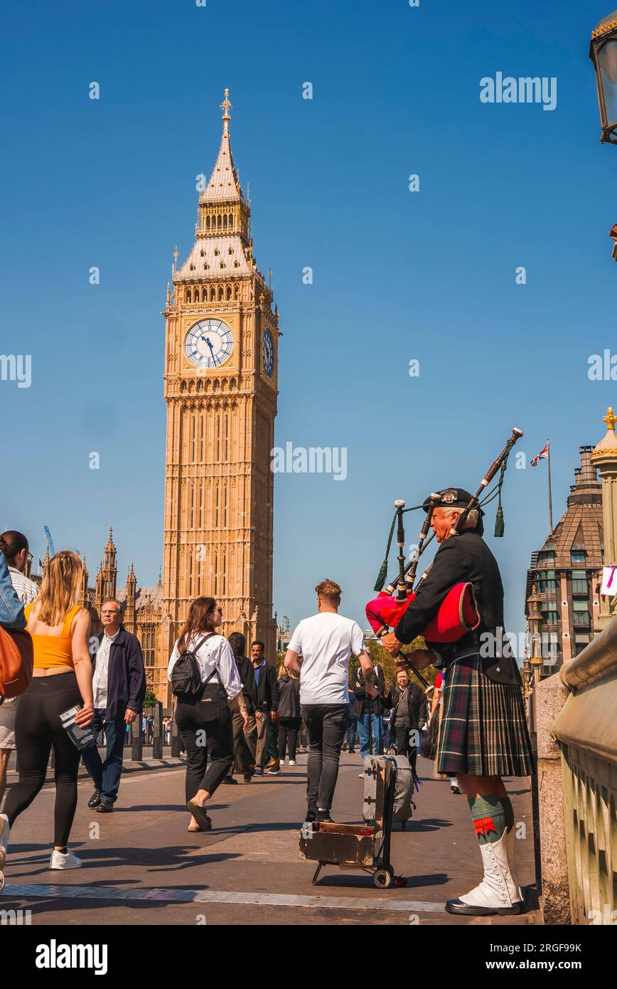 Man playing bagpipe amidst Tourists walking by Clock Tower in city Stock Photo