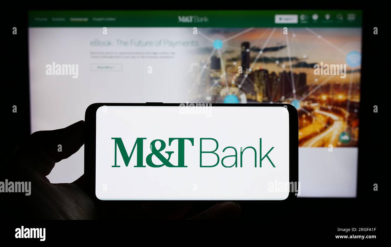 Person holding cellphone with logo of US financial company MT Bank Corporation on screen in front of business webpage. Focus on phone display. Stock Photo