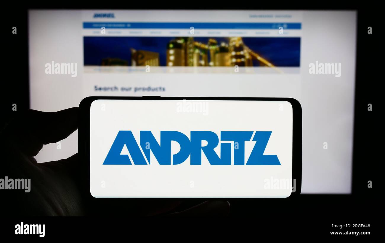 Person holding cellphone with logo of Austrian industrial company Andritz AG on screen in front of business webpage. Focus on phone display. Stock Photo