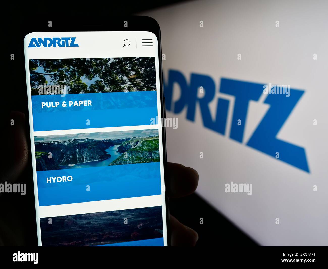 Person holding smartphone with web page of Austrian industrial company Andritz AG on screen in front of logo. Focus on center of phone display. Stock Photo