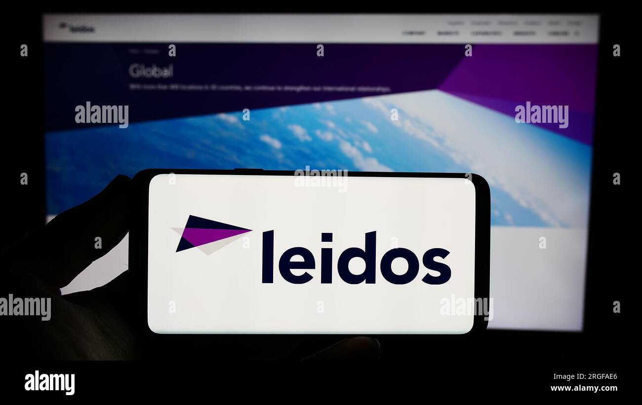 Person holding smartphone with logo of US defense company Leidos Inc. on screen in front of website. Focus on phone display. Stock Photo